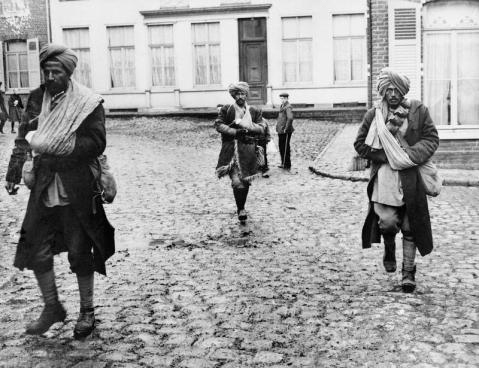 Image © IWM (Q 53348) - A group of wounded Indian soldiers walk across the cobbles of a French village.